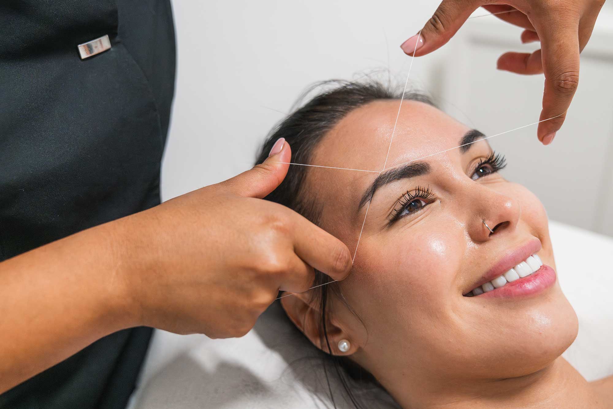 Expert esthetician performing eyebrow threading for a perfectly sculpted arch