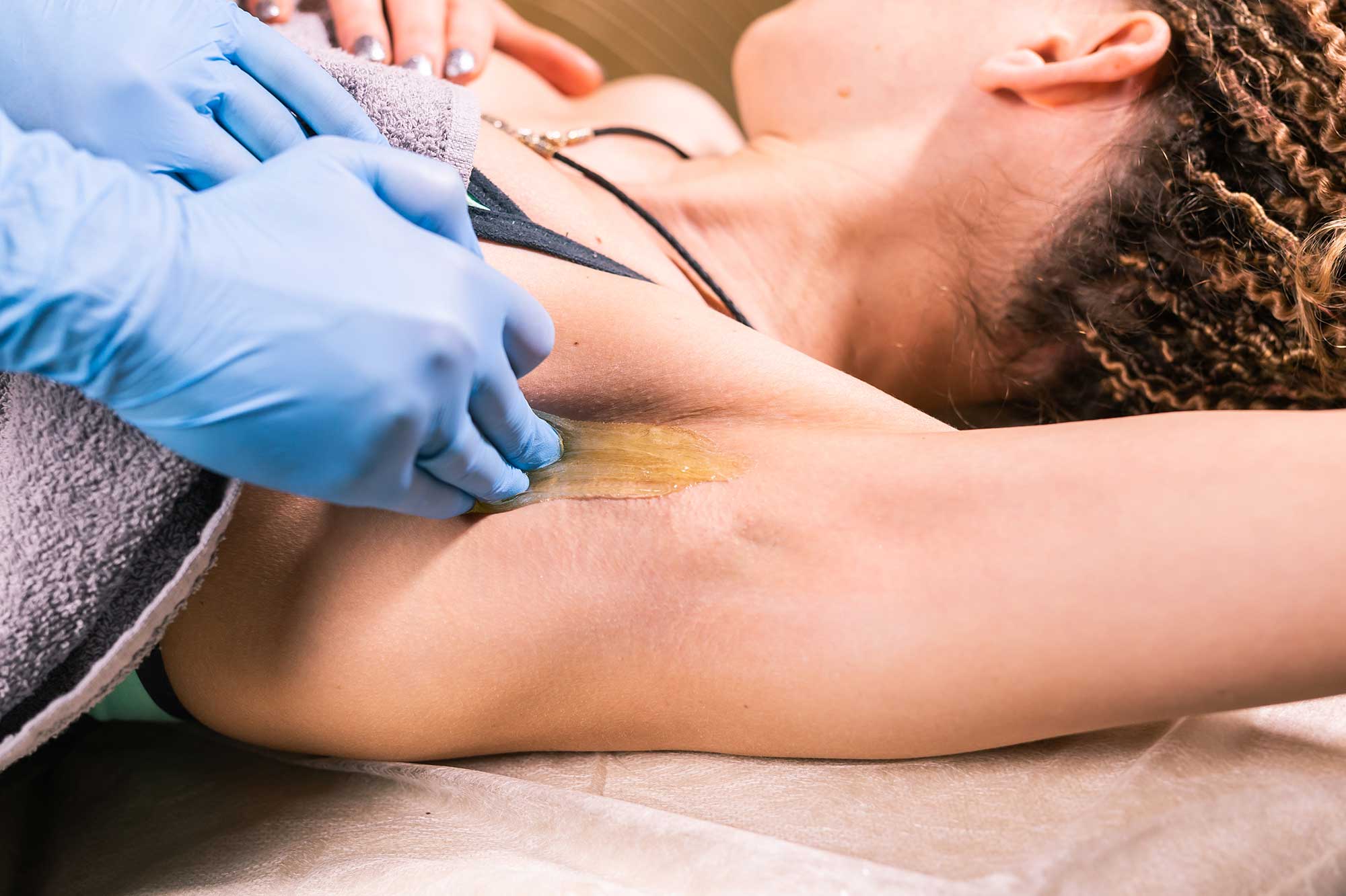 Close-up of a woman receiving professional underarm waxing at a salon.